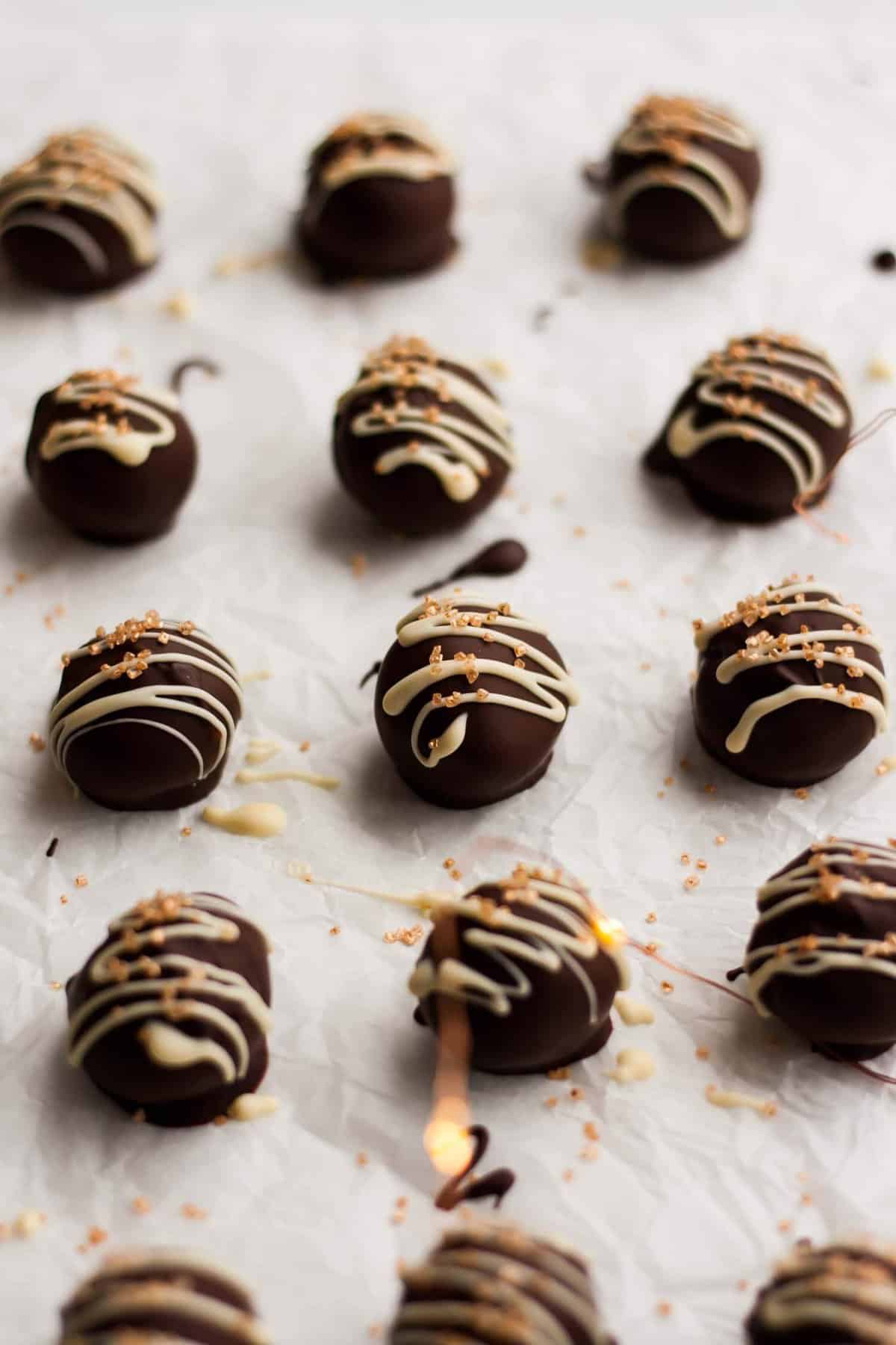 An array of twelve chocolate truffles coated in dark chocolate and white chocolate drizzle.