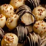 An array of white chocolate truffles decorated on a tray with one on top with a bite taken.