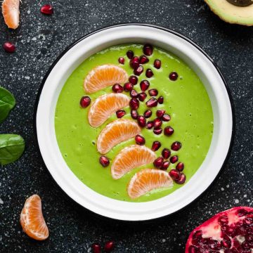 A bowl of a green smoothie topped with clementine segments and pomegranate aryls.