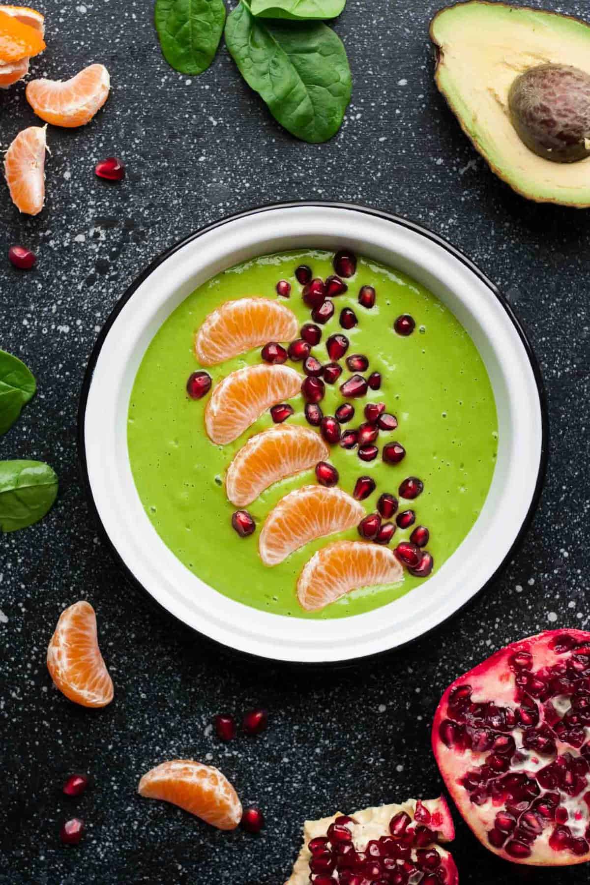 A bowl of a green smoothie topped with clementine segments and pomegranate aryls.