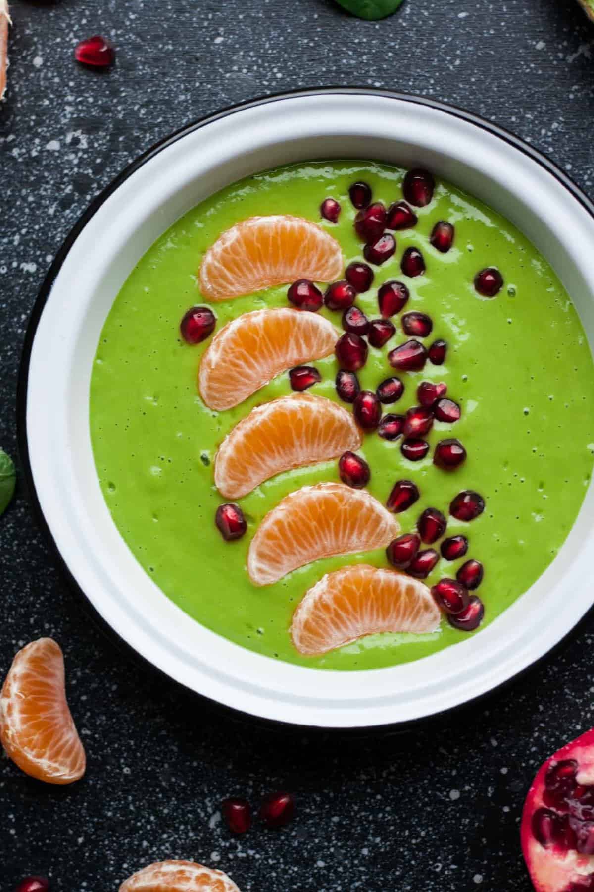 Close up of a green smoothie bowl with clementine segments and pomegranate aryls on top.