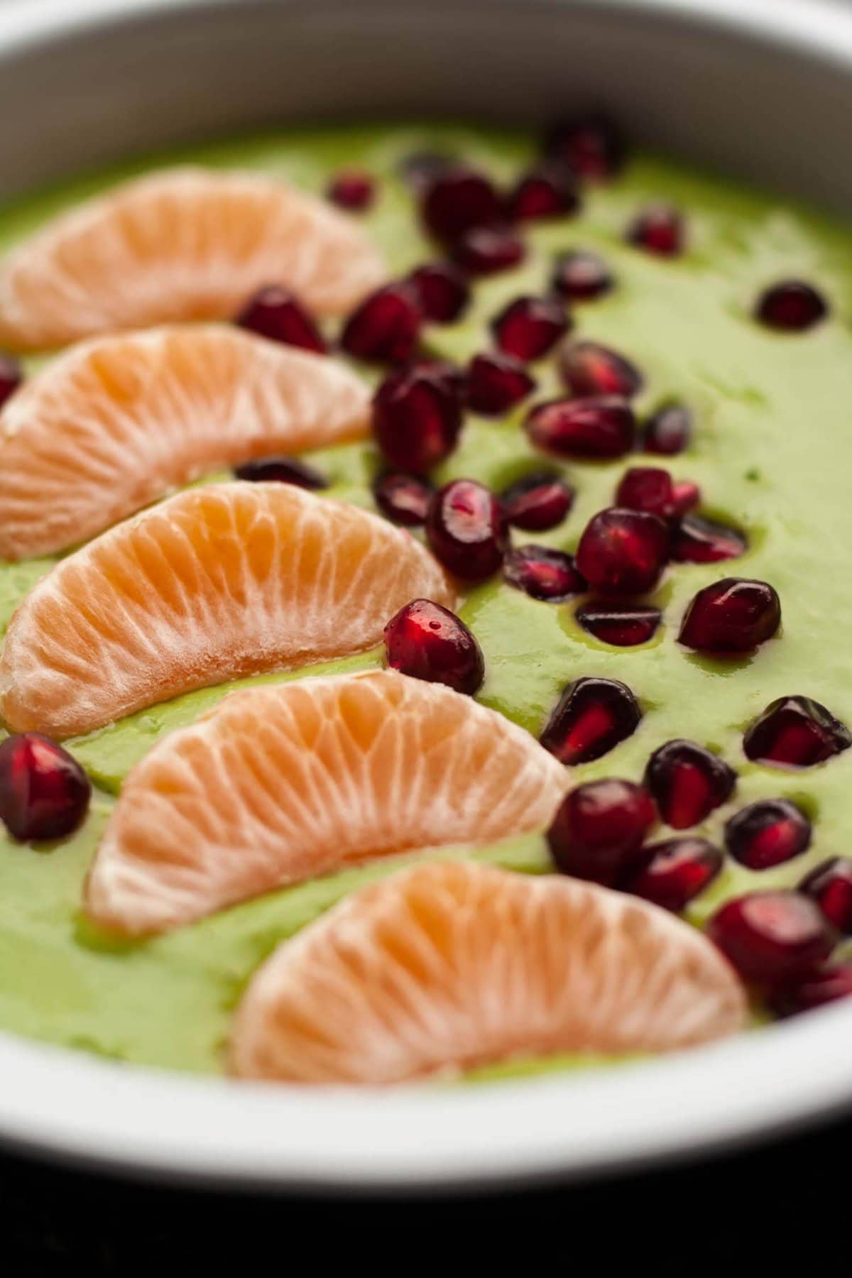An array of clementine slices and pomegranate aryls on a green liquid.