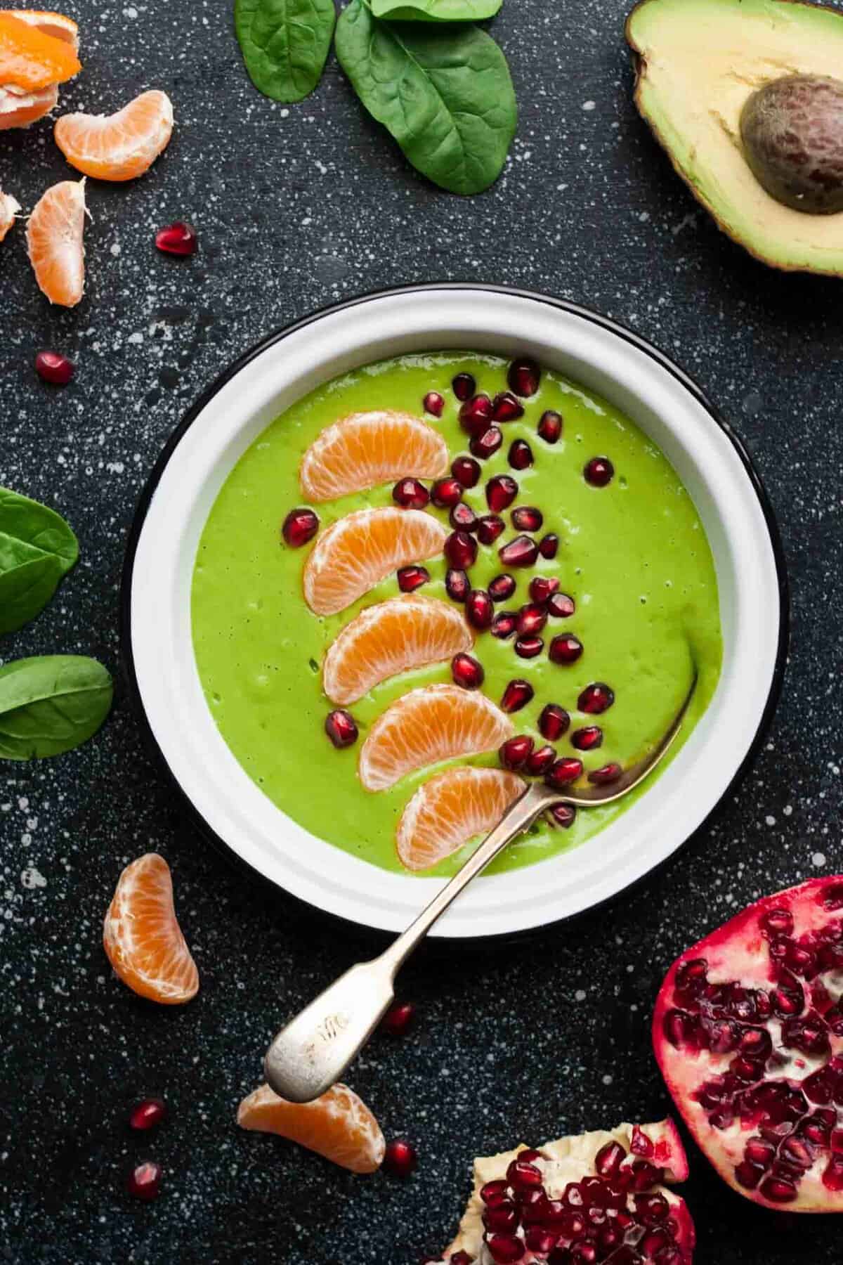 A bowl of green smoothie with fruit on top and a spoon in it.
