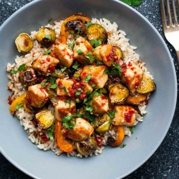 A bowl of rice topped with caramelized brussel sprouts with halloumi in a sweet chilli sauce.