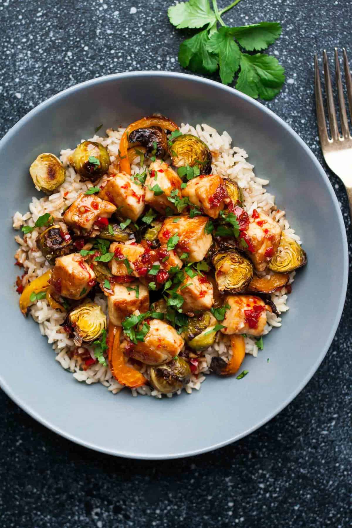 A bowl of rice topped with caramelized brussel sprouts with halloumi in a sweet chilli sauce.