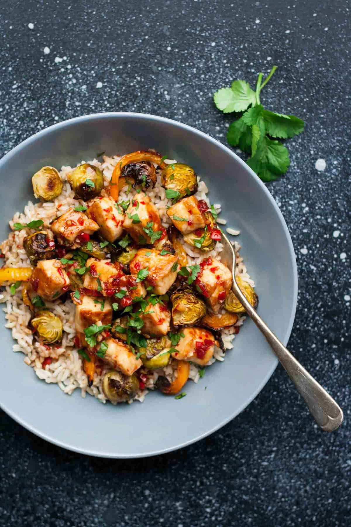 Crispy brussels sprouts with halloumi and chilli sauce over a bed of rice in a bowl with a fork.