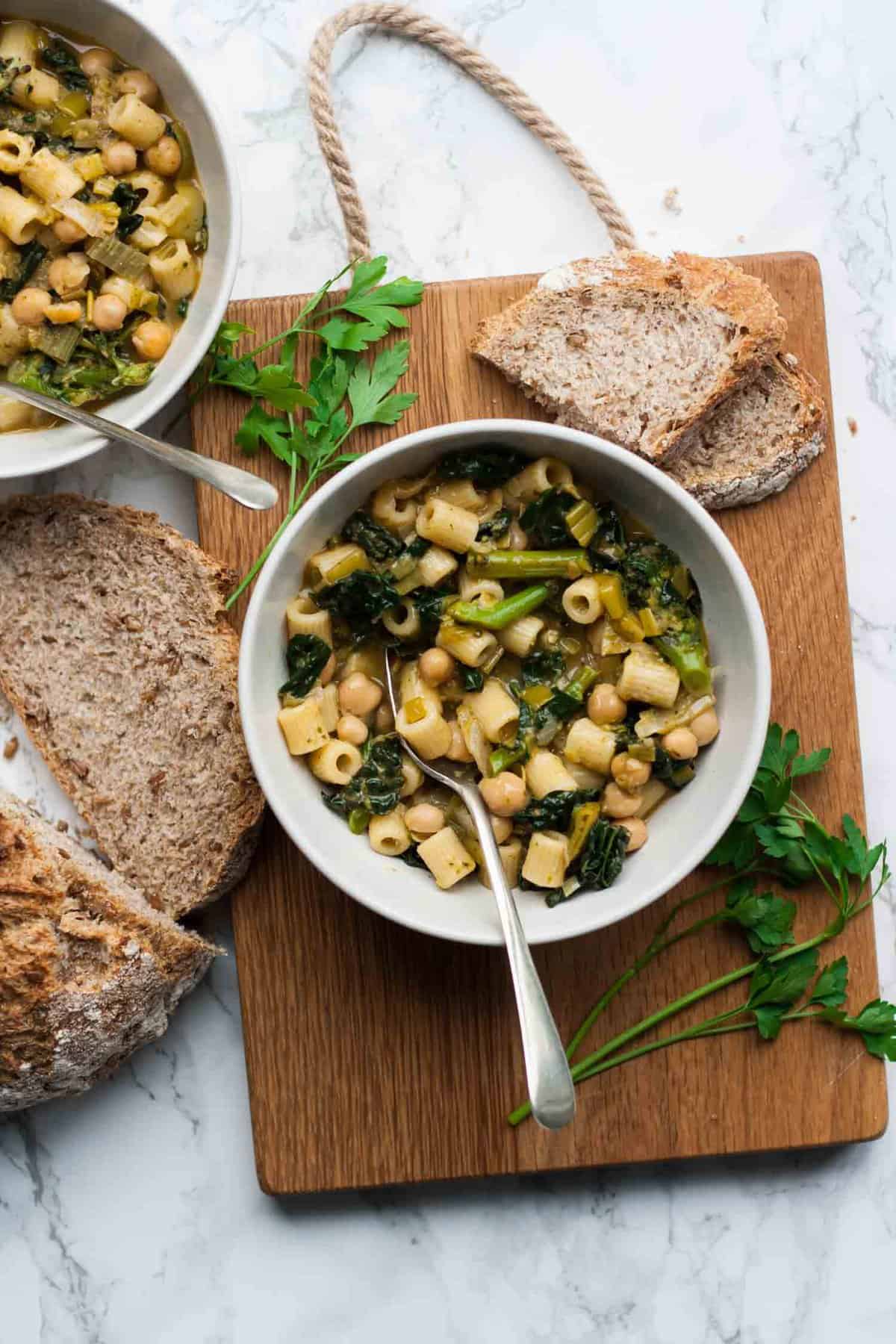 A bowl of pasta and chermoula sitting on top of a wooden board with a spoon and bread. 