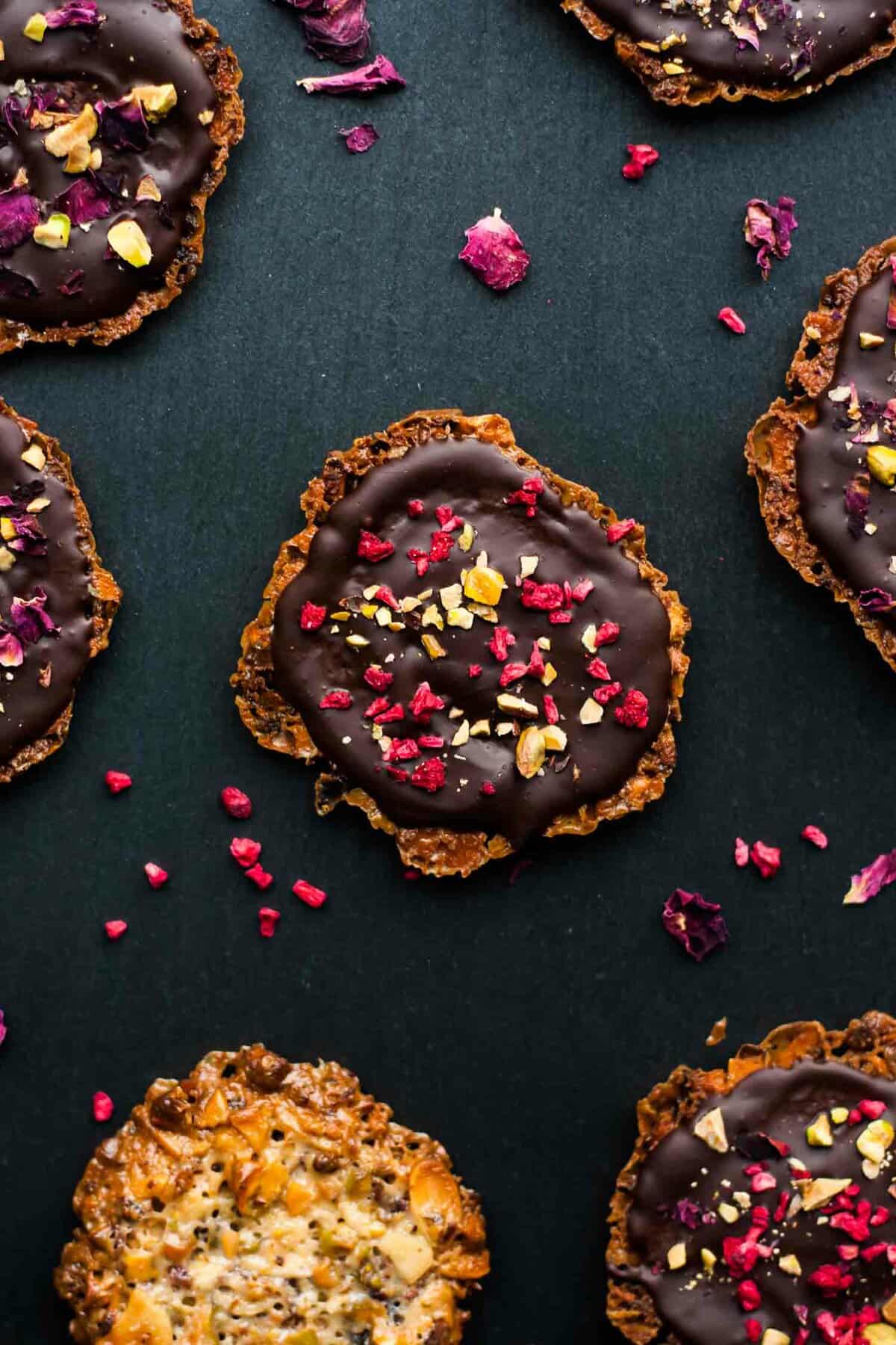 An array of chocolate almond florentines with rose petals around.
