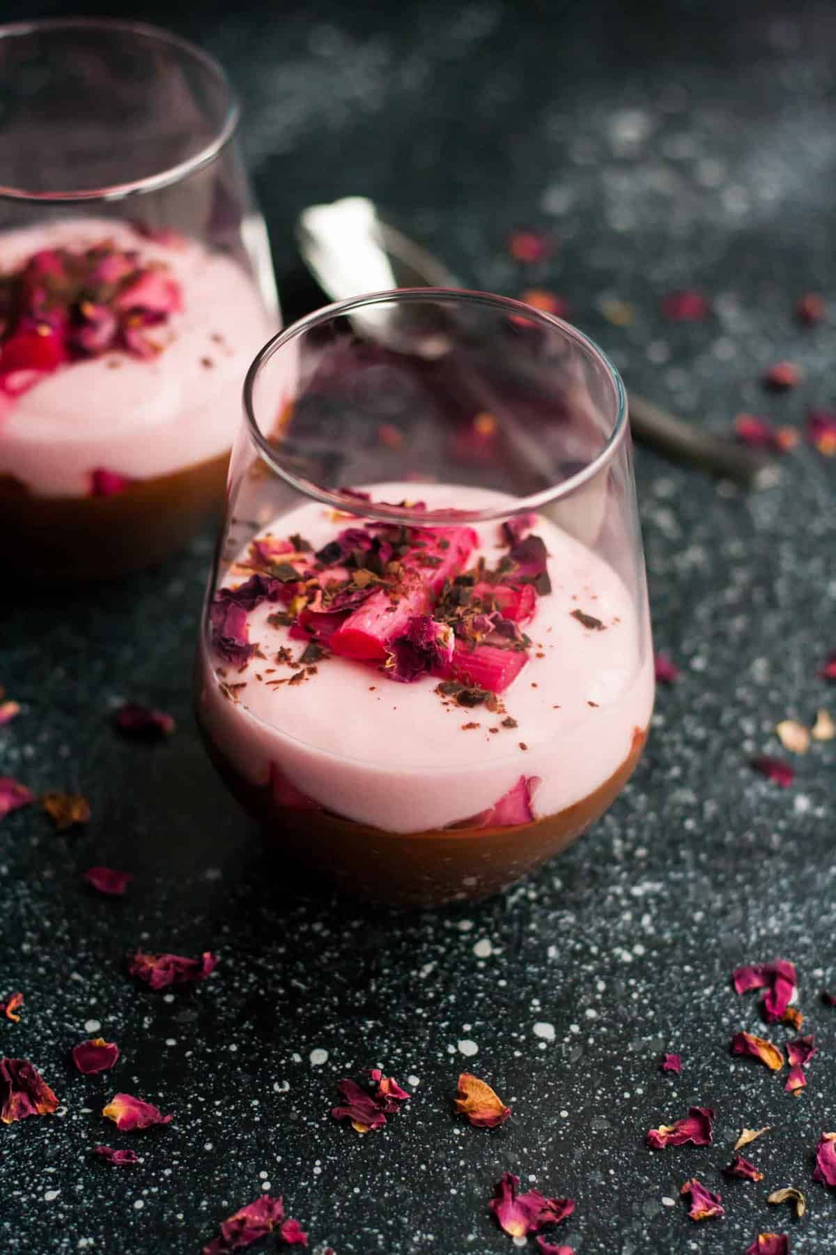 A close up of two glasses of rhubarb and chocolate parfait with a spoon behind.