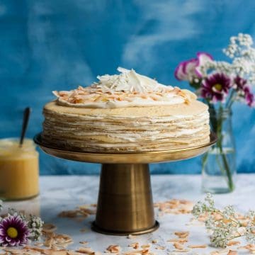 A crepe cake on a cake stand with a jar of lemon curd in the background.