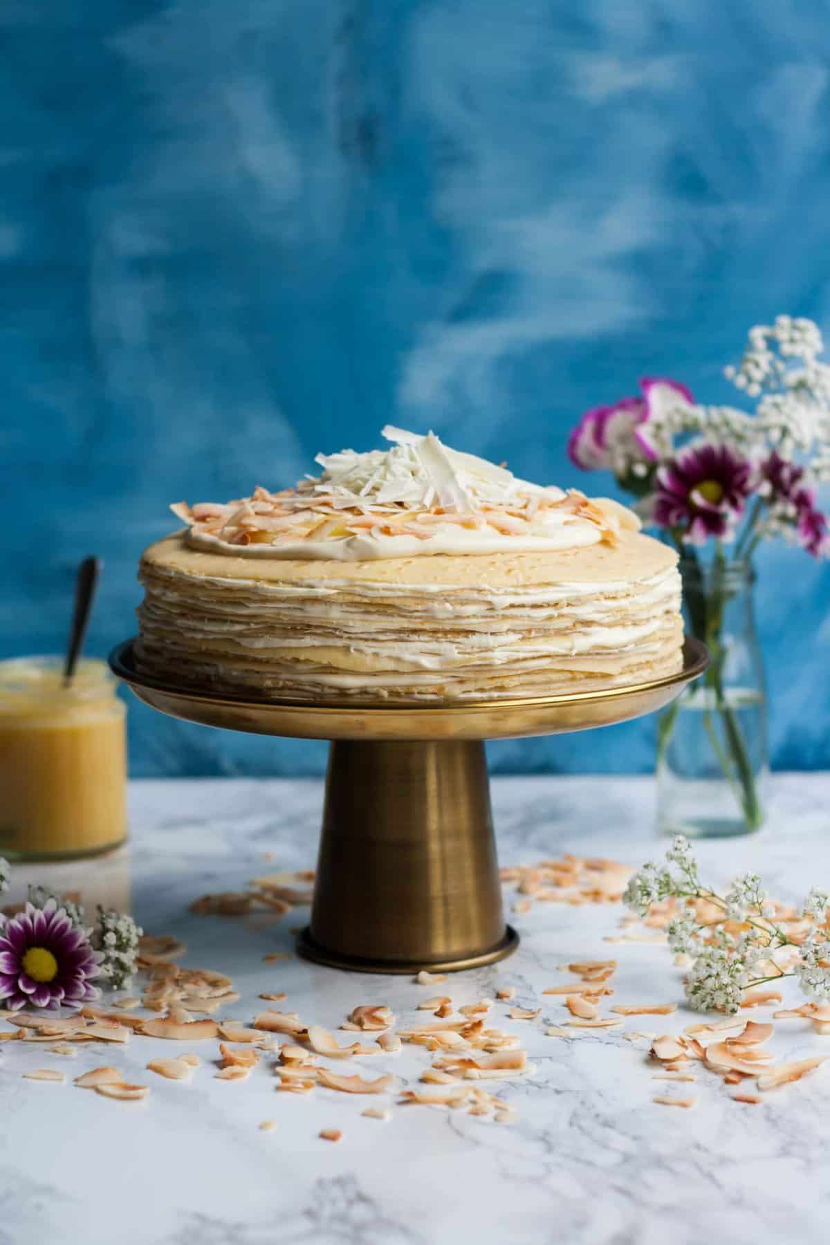 A crepe cake on a cake stand with a jar of lemon curd in the background.