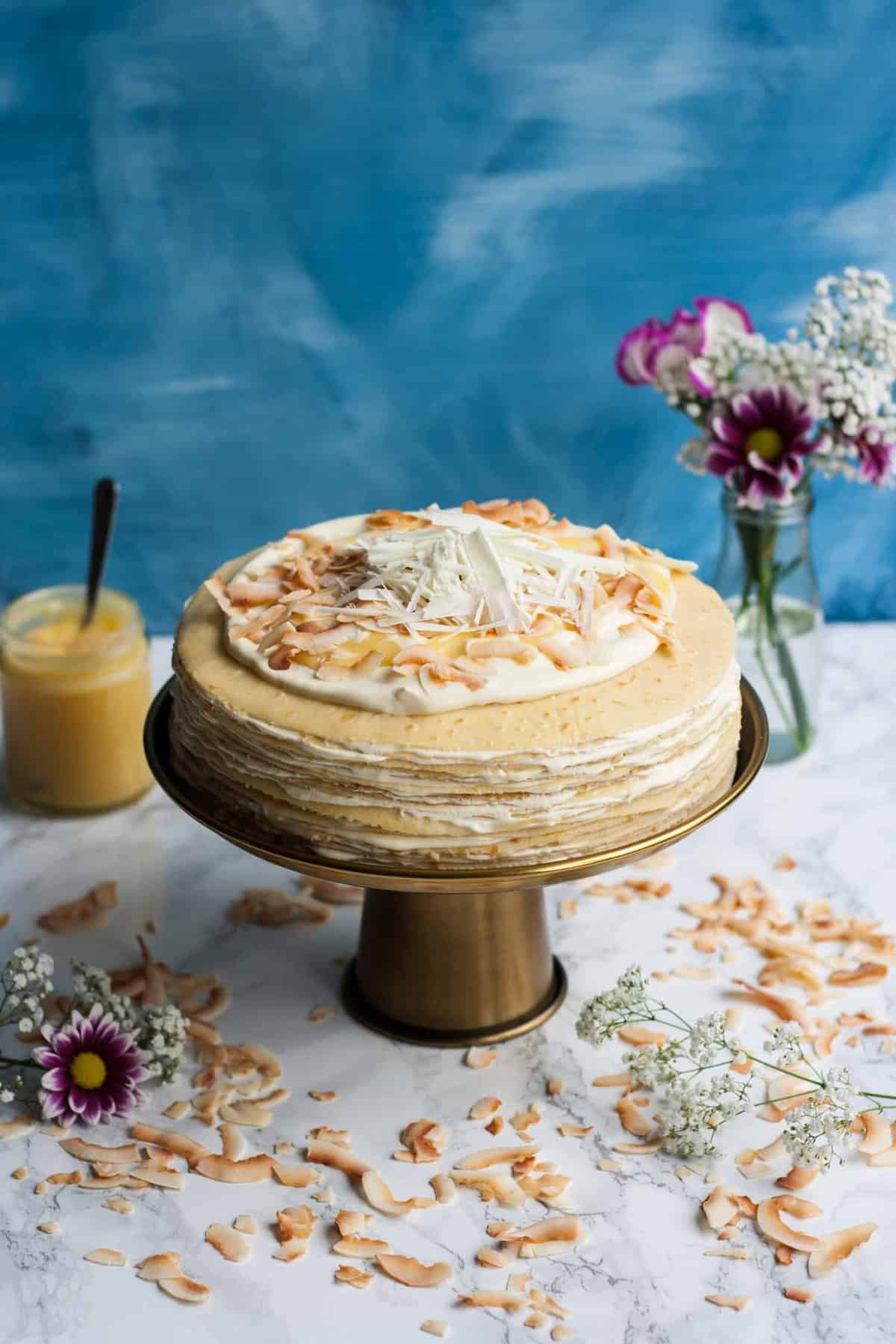 A cake sitting on top of a cake stand with flowers and lemon curd.