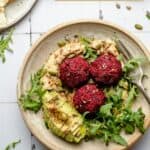 Beetroot falafel in a bowl with hummus, pitta, avocado and some arugula.