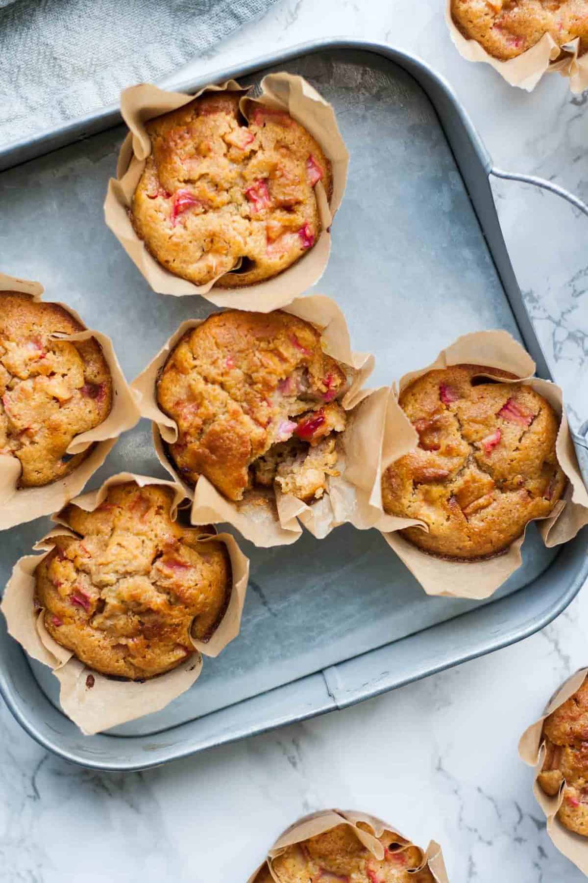 A selection of rhubarb muffins with one broken open in a tin tray.