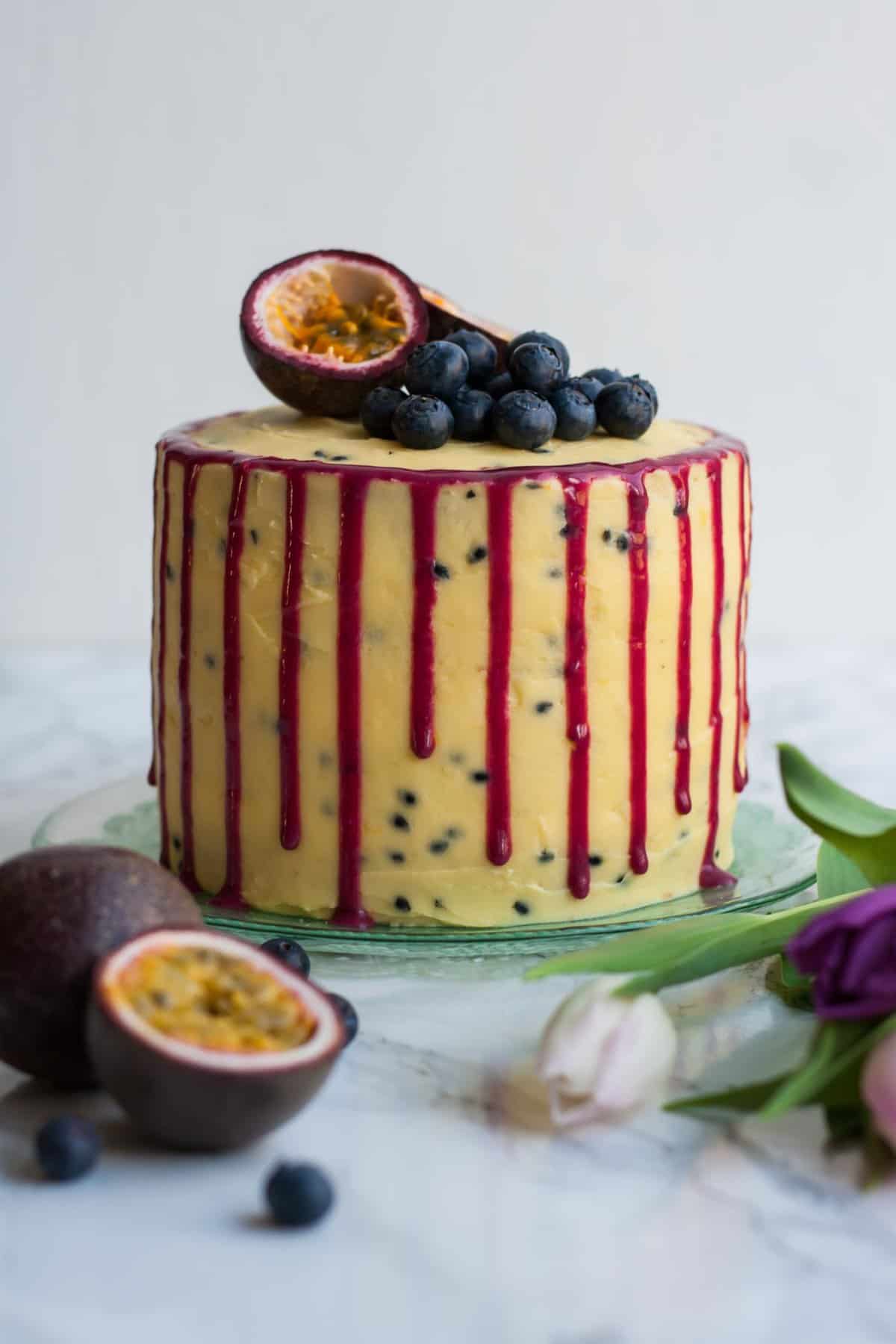 A cake plate with blueberry passionfruit cake with a drizzle down the side.