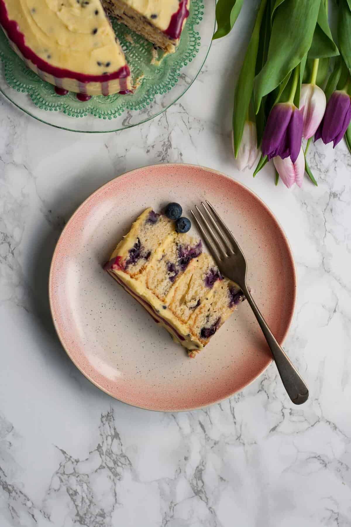 A piece of cake on a plate with a fork and some flowers nearby.