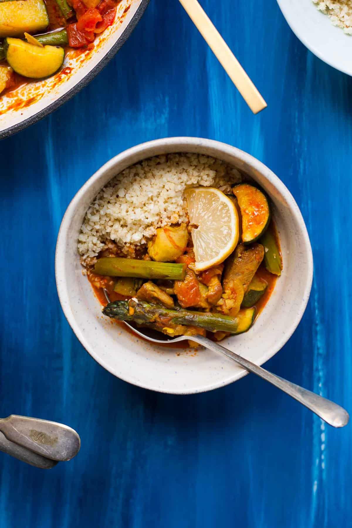 A bowl of chicken vegetable tagine with couscous and a spoon.