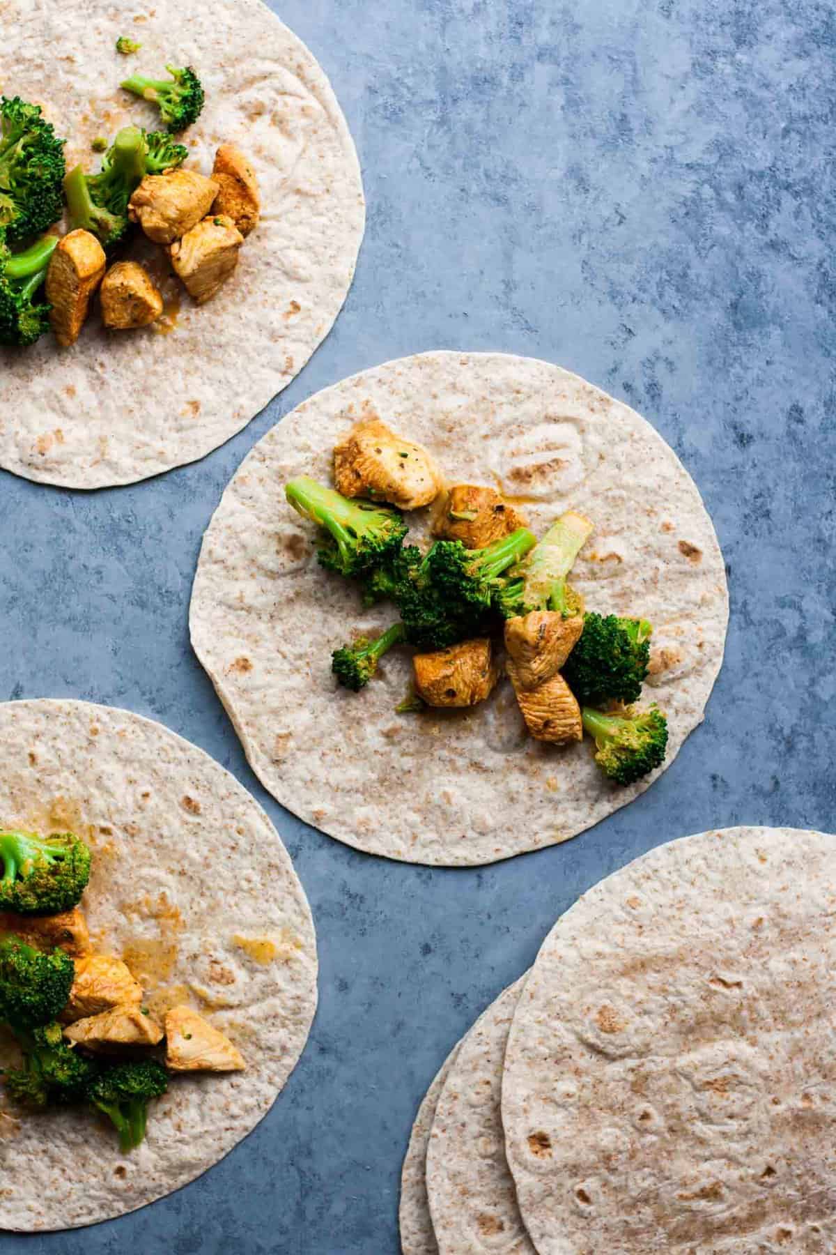 A tortilla with chicken and broccoli on top before wrapping. 