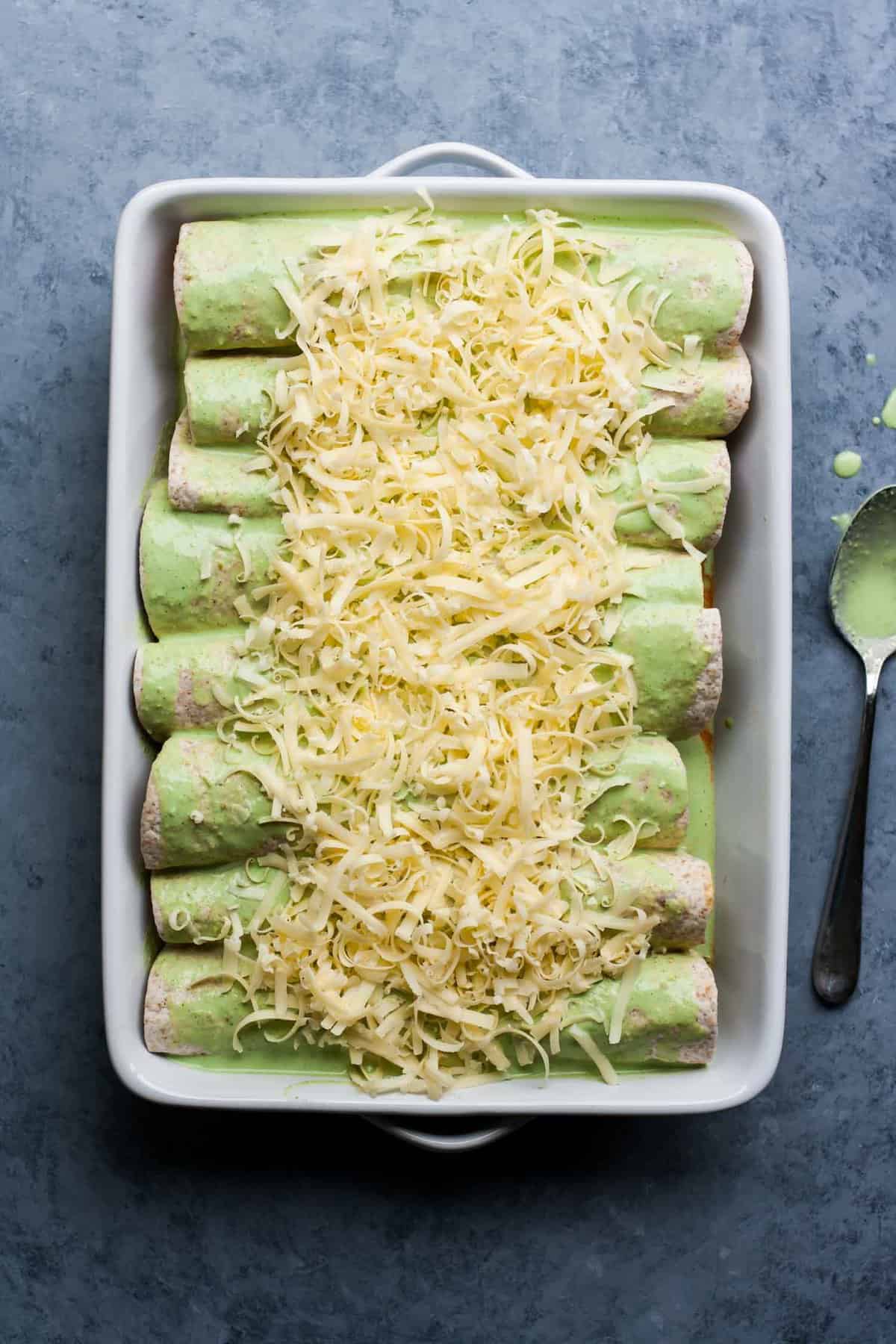 A pre-baked baking dish full of enchiladas with cheese on top.