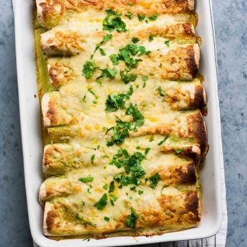 Enchiladas baked in a dish with cheese and herbs on top.