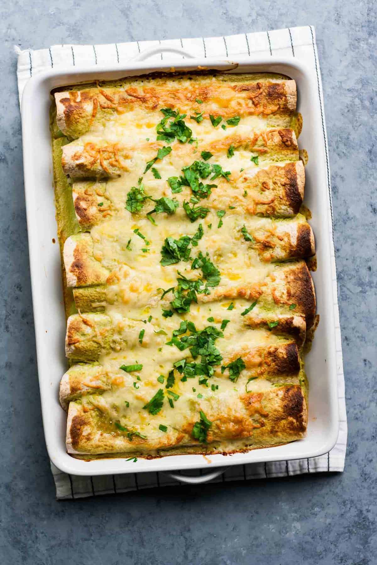 Enchiladas baked in a dish with cheese and herbs on top.