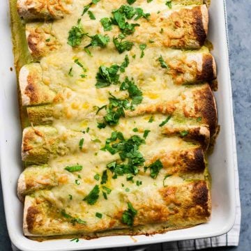 A baking dish with enchiladas with cheese melted on top with chopped herbs.