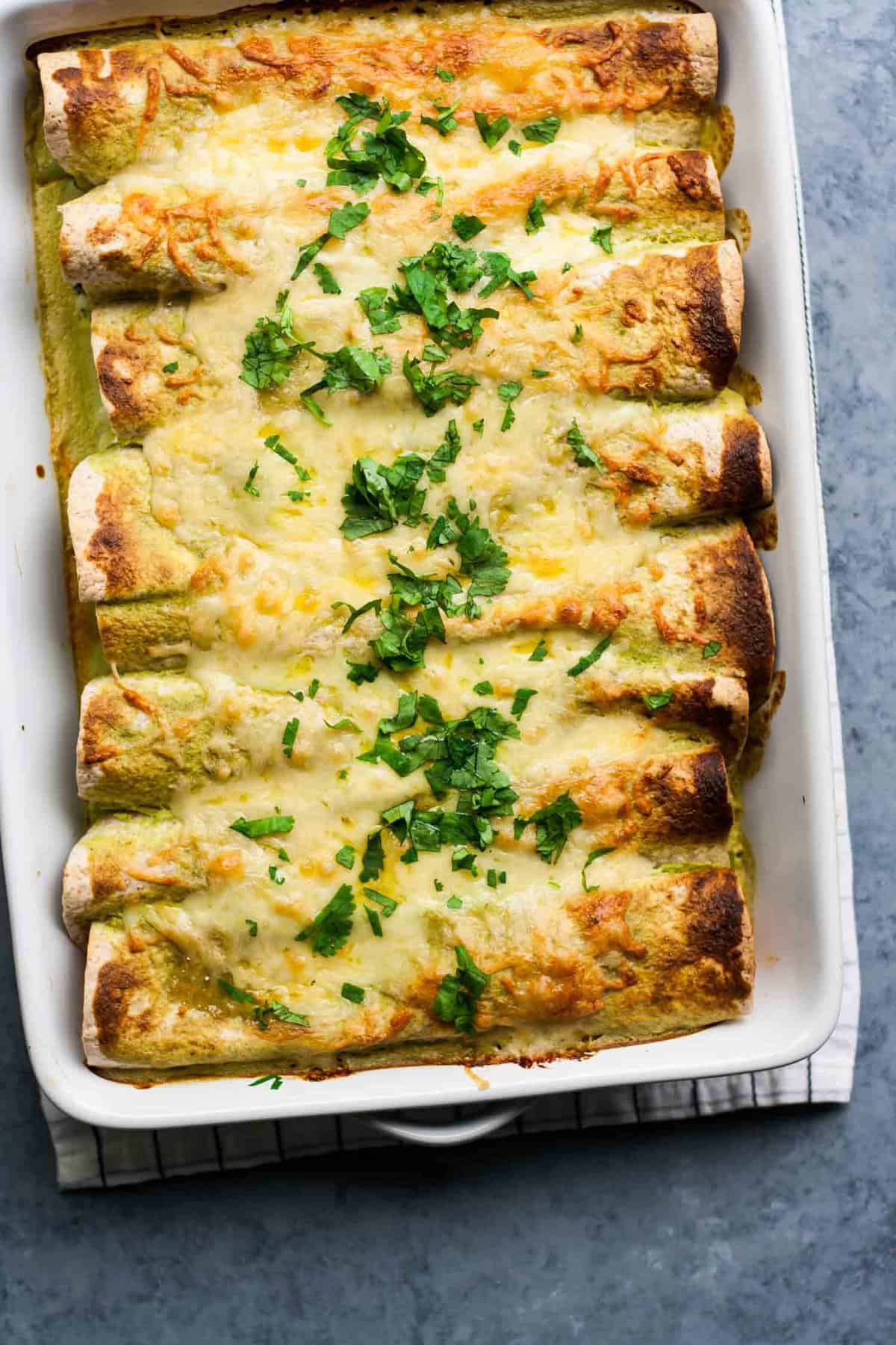 A baking dish with enchiladas with cheese melted on top with chopped herbs.