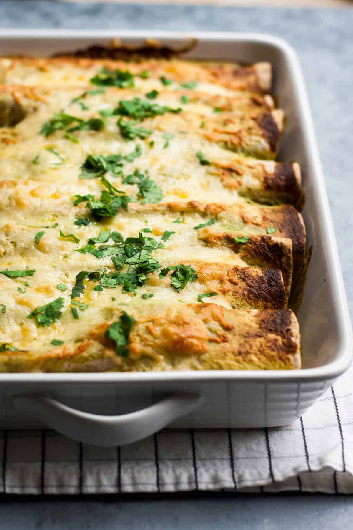 A baking dish with enchiladas with green sauce. 