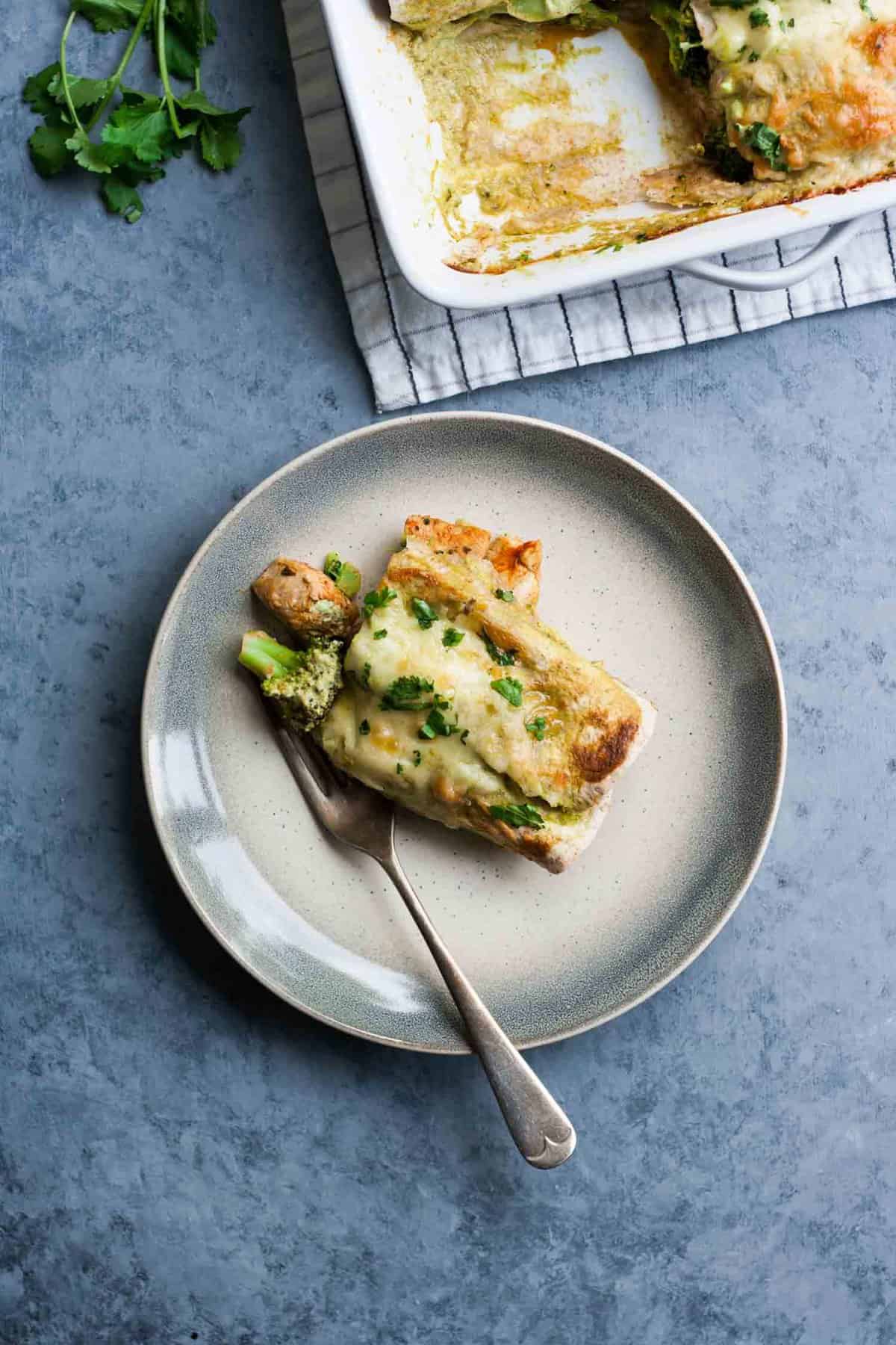 A plate of green chicken enchiladas with broccoli. 