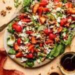 strawberry salad served on a platter with a fork and a bowl of balsamic dressing to the side.