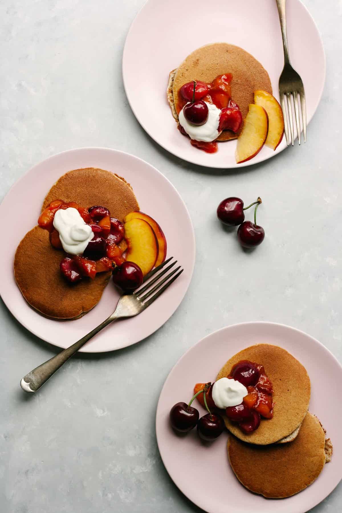 Almond Butter Pancakes on plates with fruit and yoghurt.