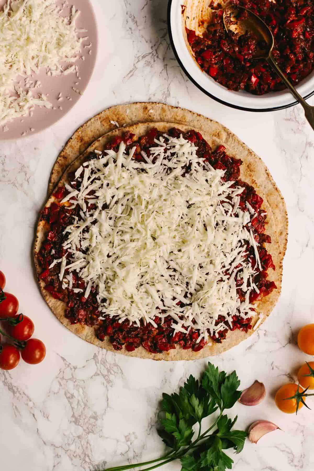 Grated halloumi on top of harissa on a flatbread with tomatoes nearby.