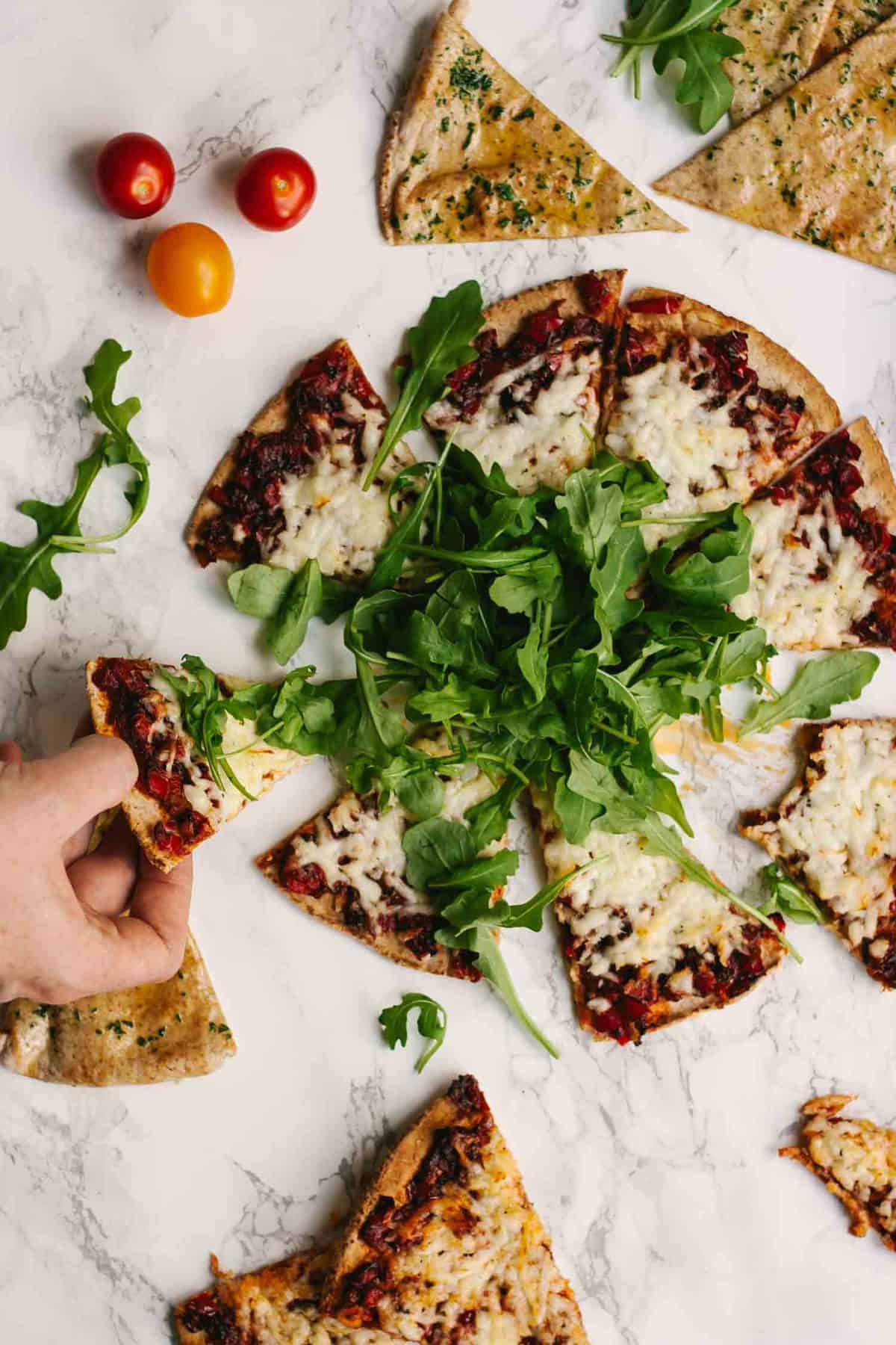 A halloumi flatbread cut into slices and a hand taking one. 