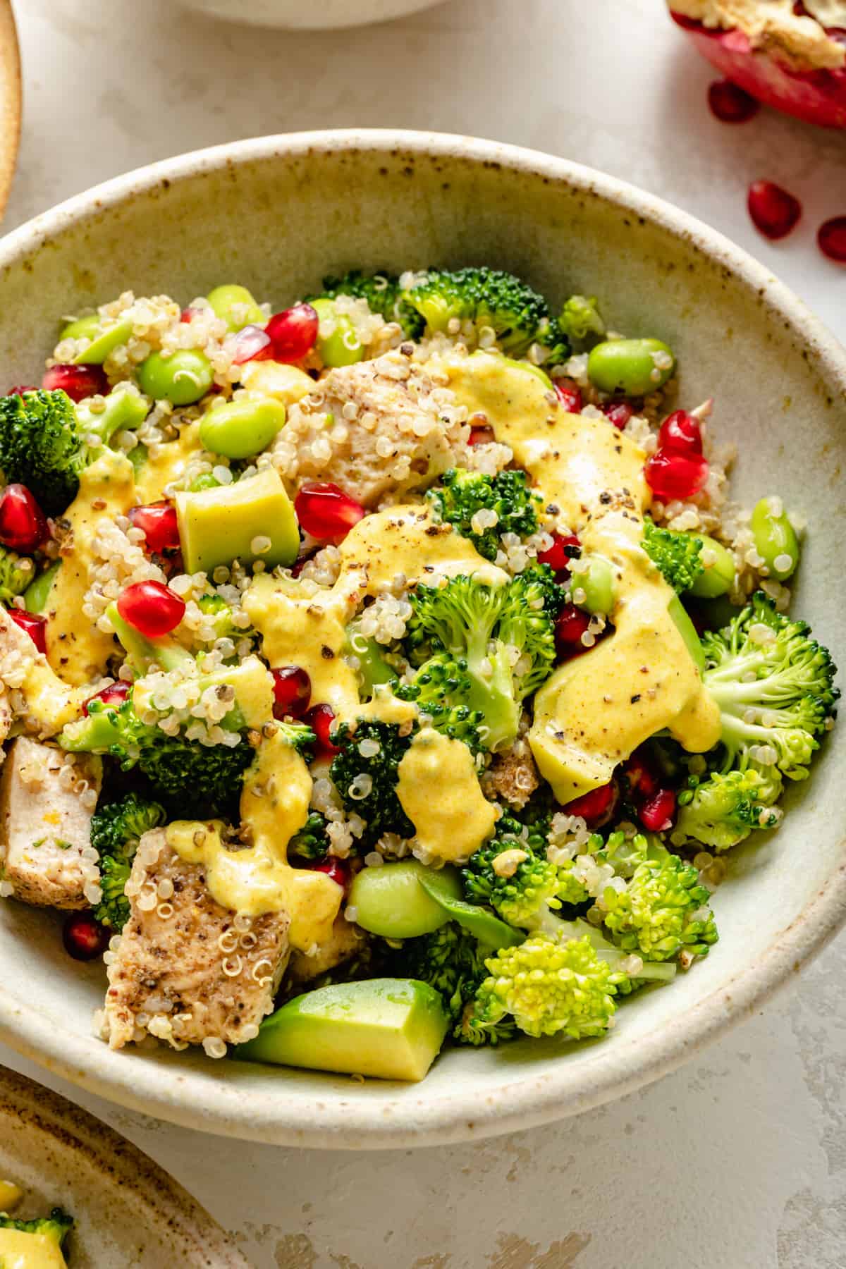 Chicken quinoa salad in a bowl showing broccoli, avocado and pomegranate arils.