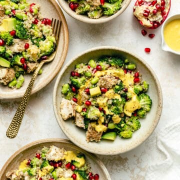 chicken quinoa salad in various bowls with gold fork and pomegranate broken open and a small jug of turmeric dressing.