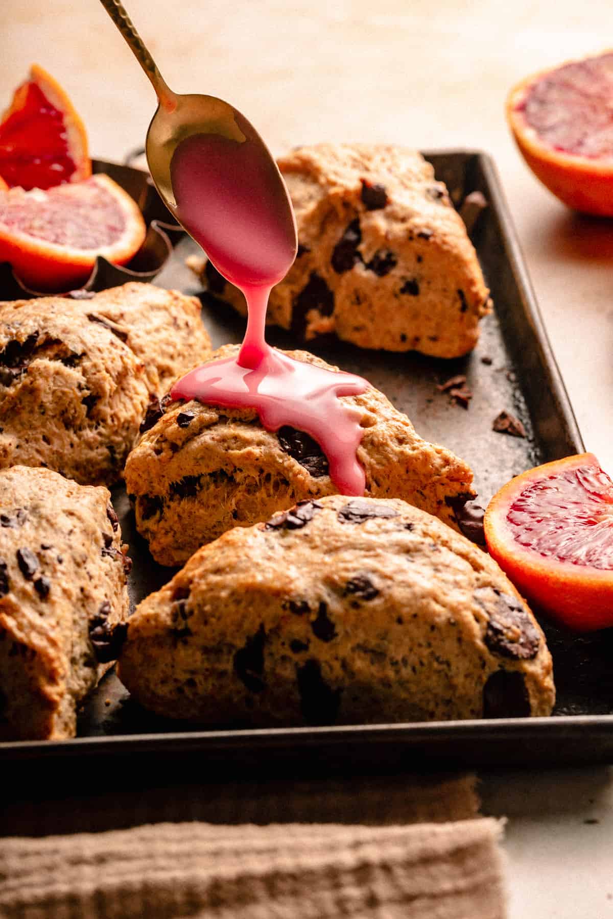 Chocolate Chip Scones on a baking sheet having blood orange glaze drizzled over the tops with a spoon.