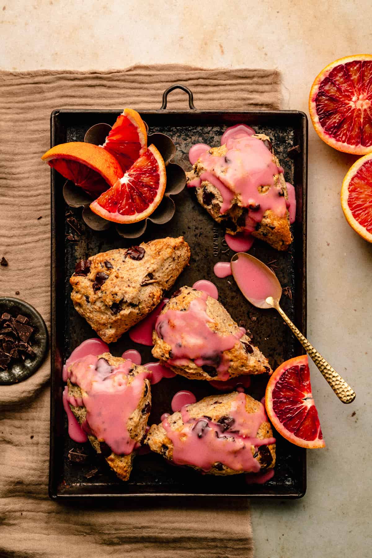 Chocolate Chip Scones with blood orange glaze on a sheet pan with wedges of blood orange around.