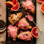 Chocolate Chip Scones with blood orange glaze on a sheet pan with wedges of blood orange around.