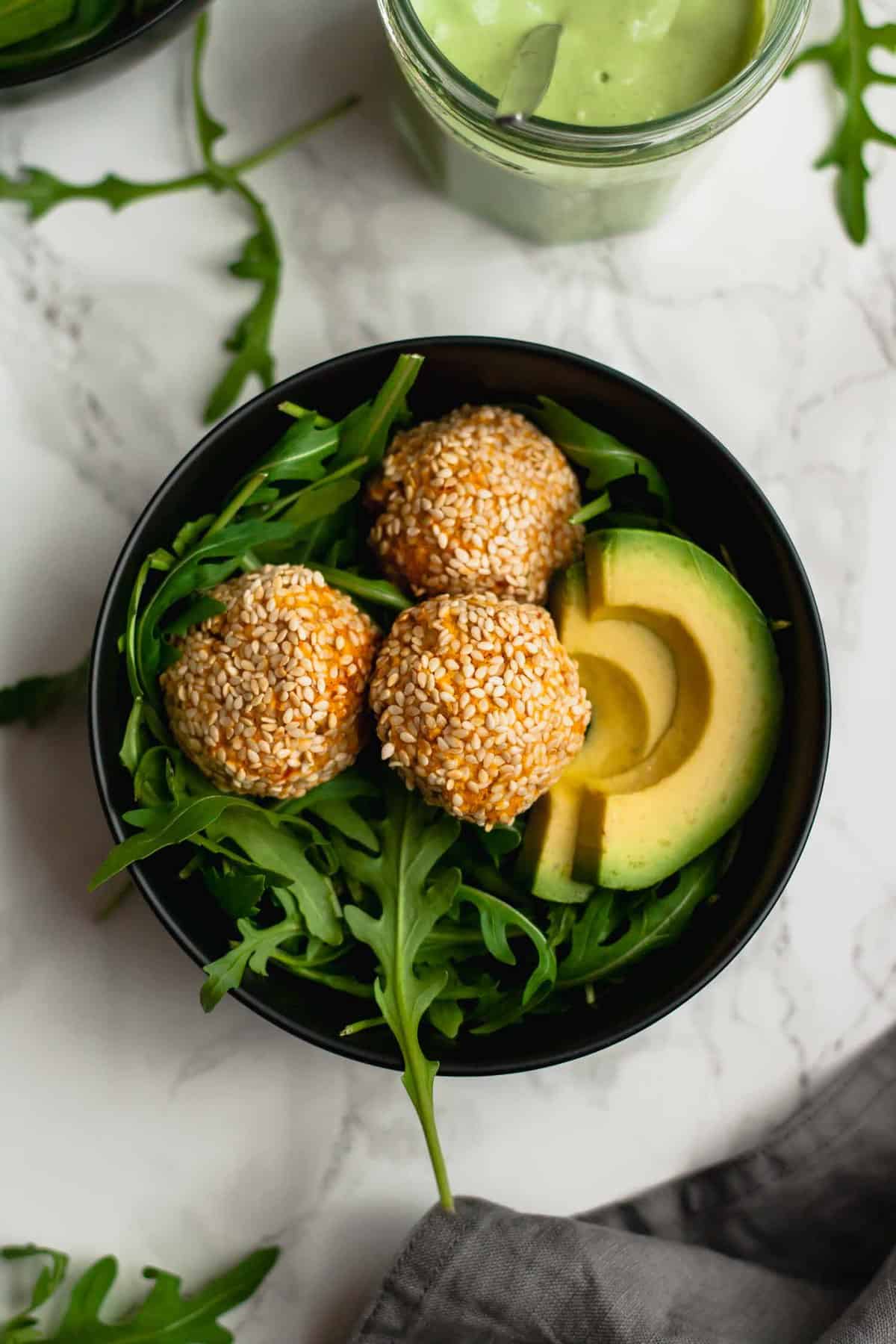 A bowl with arugula, sweet potato falafel and avocado.