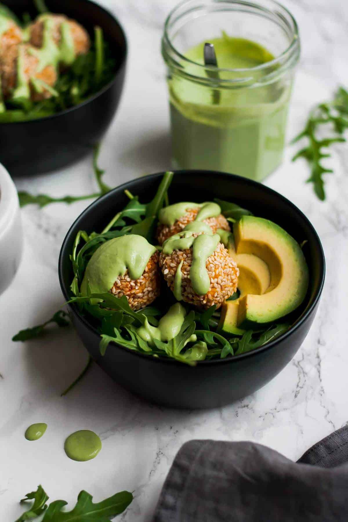 A bowl with sweet potato falafel and jar of sauce behind. 