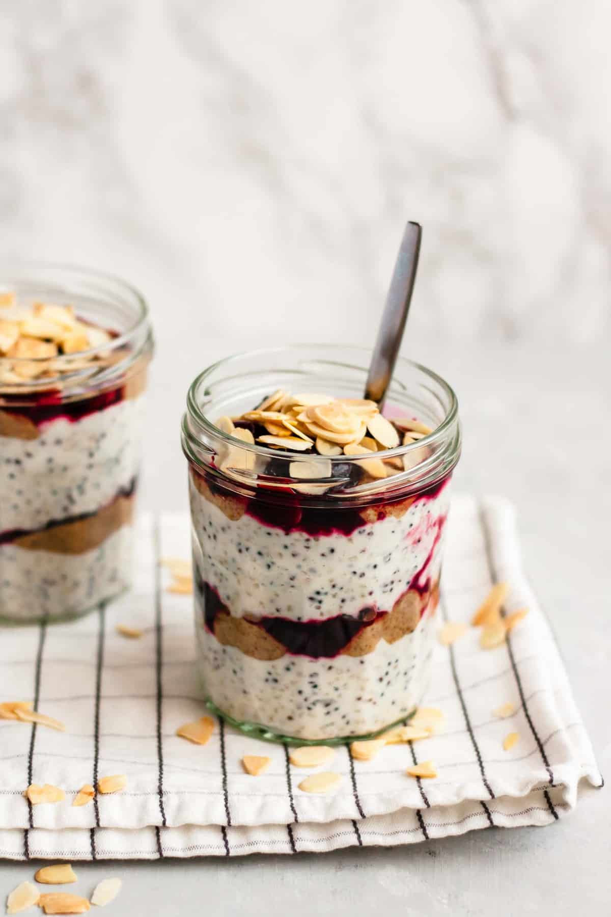 Two jars of breakfast parfait with almond flakes and spoons.