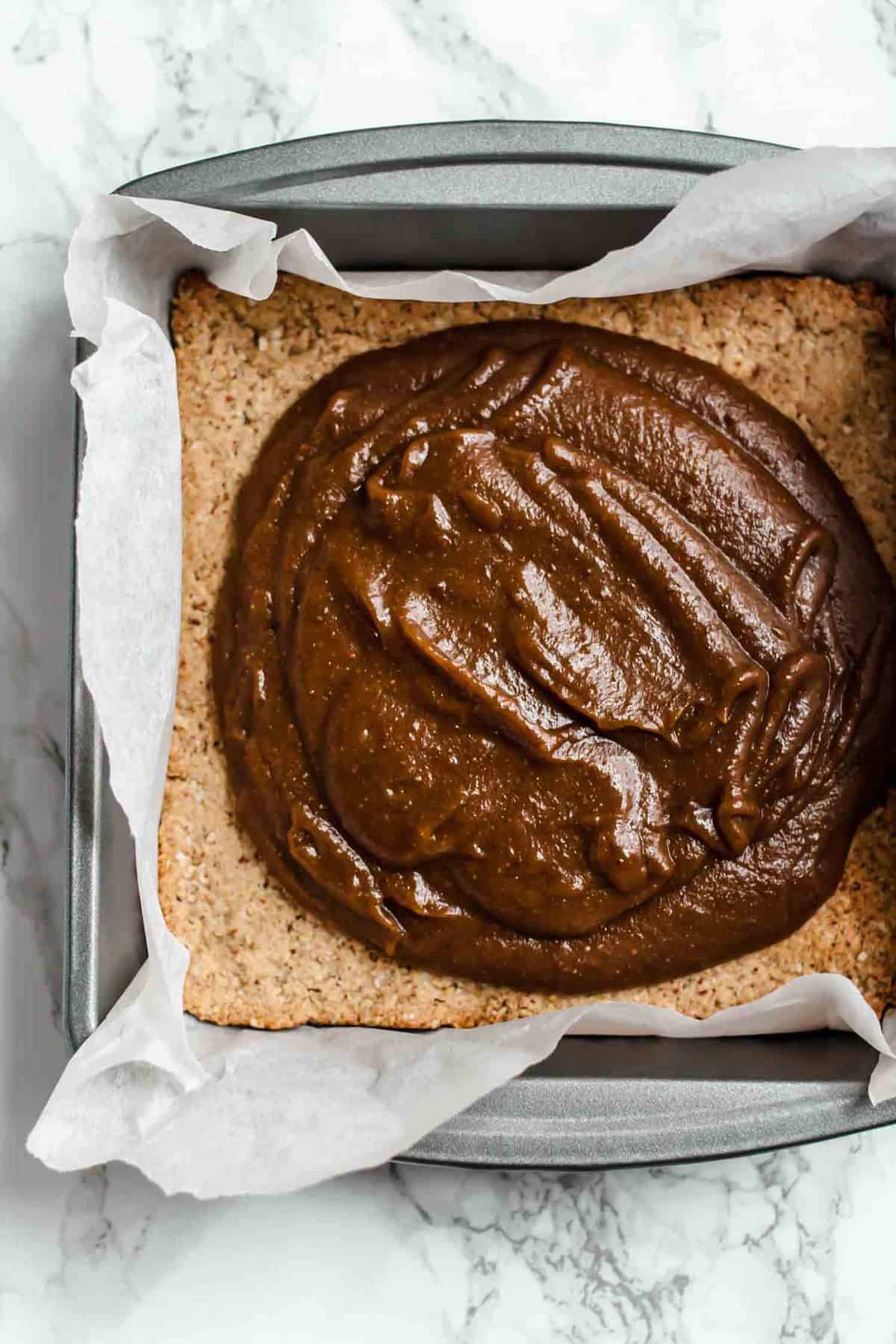 Process of spreading vegan caramel on biscuit base in a tin.