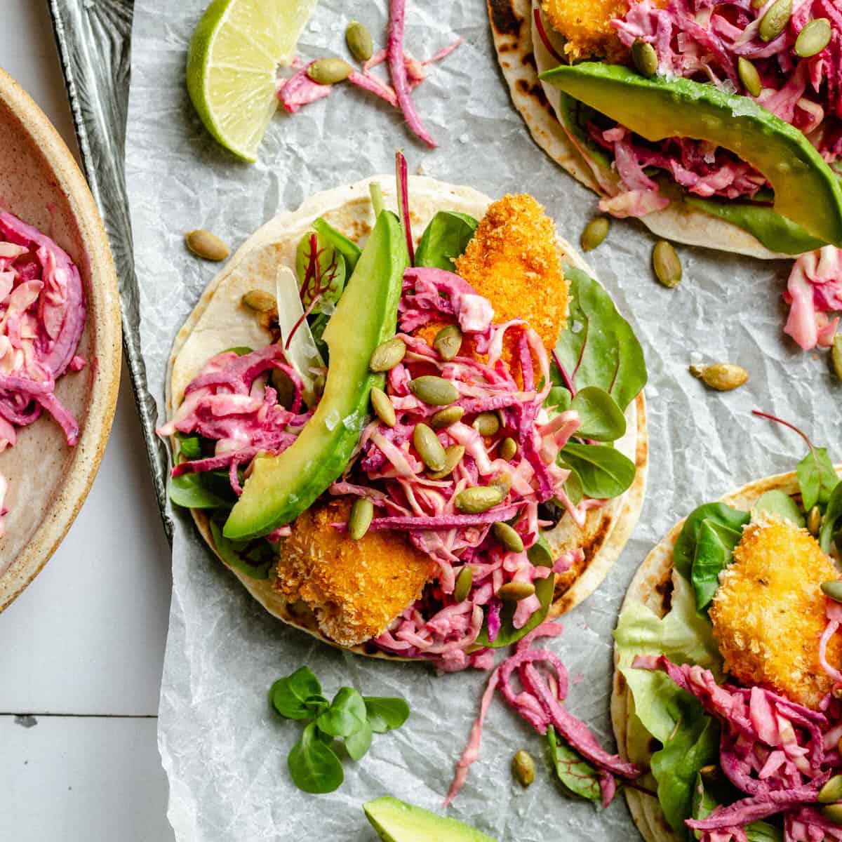 three crispy chicken tacos on parchment paper with beet slaw on top. 