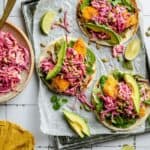 Crispy chicken tacos assembled on a tray lined with parchment and a bowl of slaw to the side.