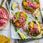 Crispy chicken tacos assembled on a tray lined with parchment and a bowl of slaw to the side.