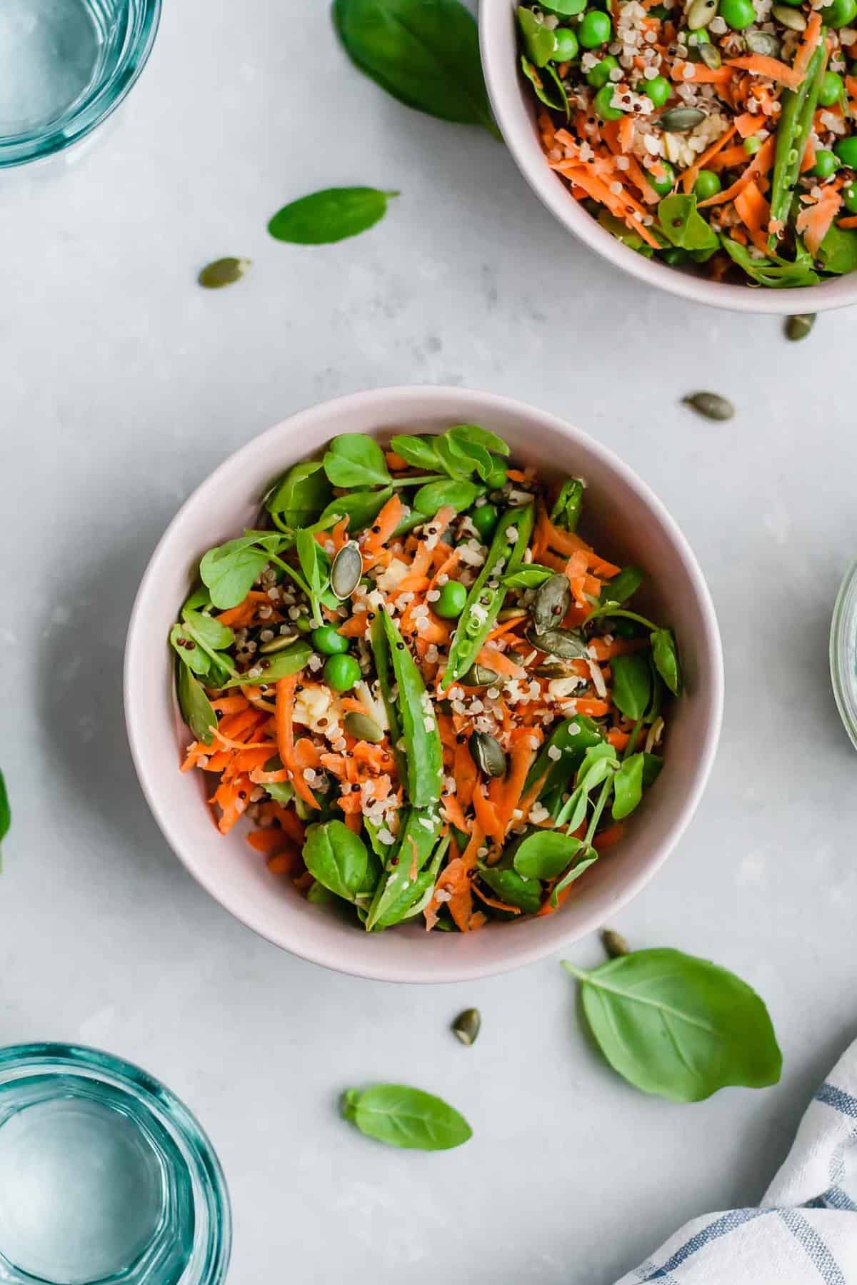 A bowl with Pea and Quinoa salad with some basil leaves around.