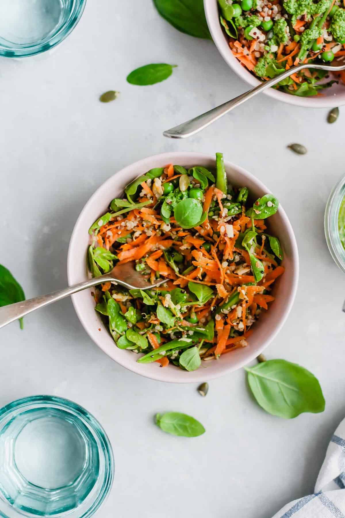 A bowl of quinoa salad with a fork and a glass of water nearby.