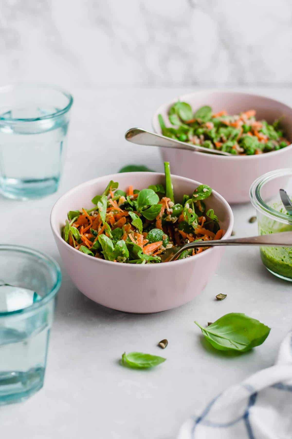 two bowls of salad with forks and glasses of water and a jar of pesto.