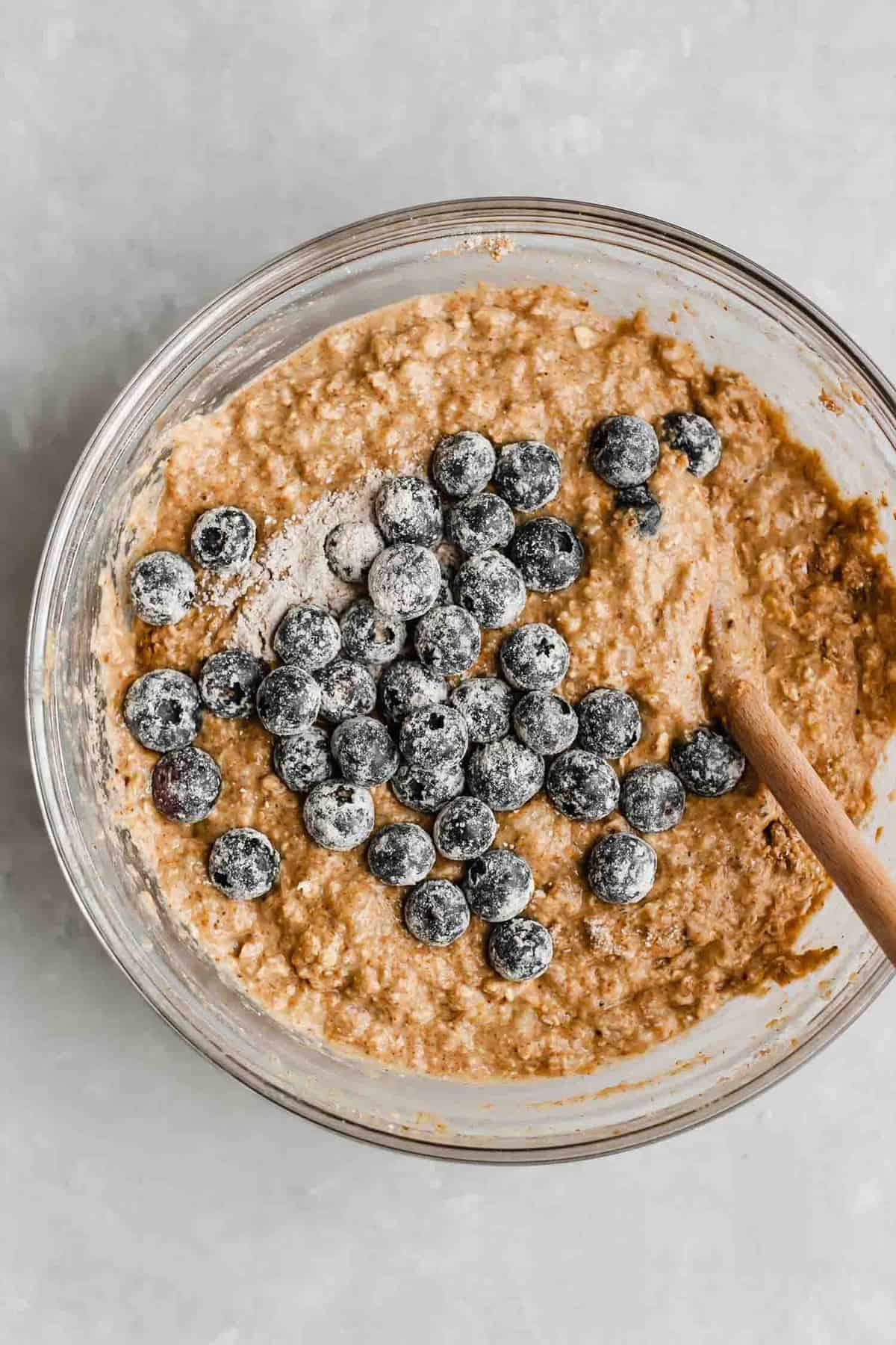 Vegan blueberry muffins batter in a bowl with blueberries being stirred in.