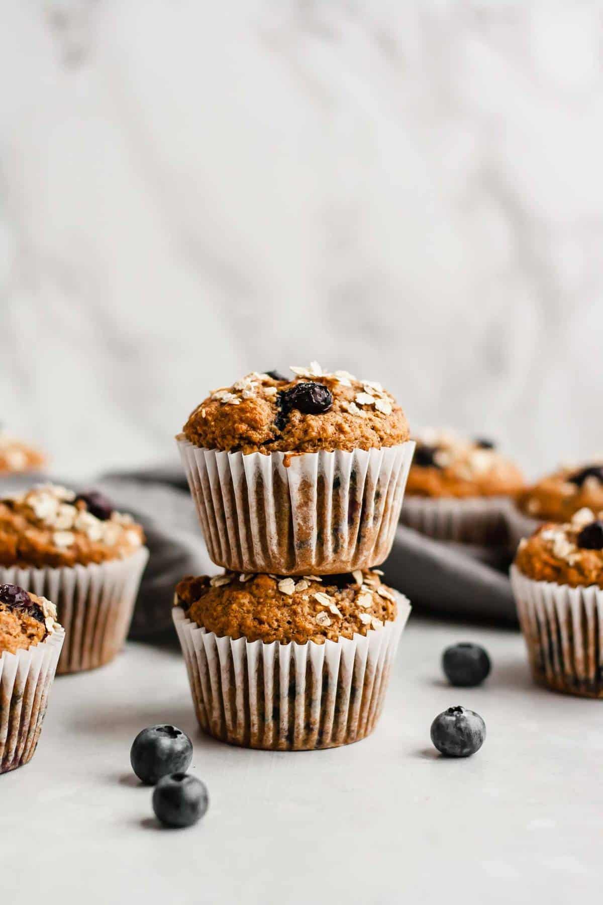 Stacked blueberry muffins with blueberries around nearby.